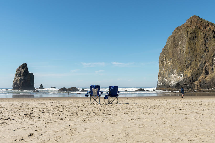 Two Blue Folding Chairs In The Sand As A Tourist Strolls Along Tcannon Beach, Oregon, Usa - October Photograph