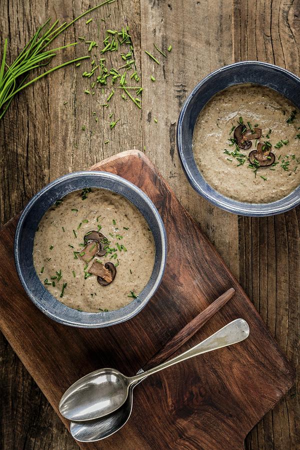 Two Bowls Of Thick And Creamy Mushroom Soup Garnished With Mushroom Slices And Chives In Blue Bowls On A Wooden Surface Photograph by Sarah Coghill