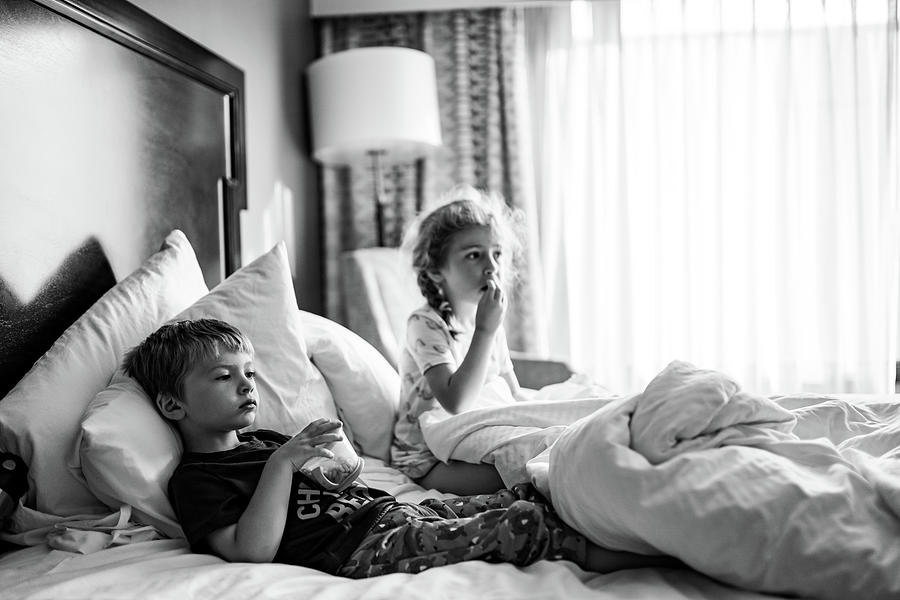 Snack Photograph - Two Children Lie In A Hotel Room Bed Eating Snacks. by Cavan Images