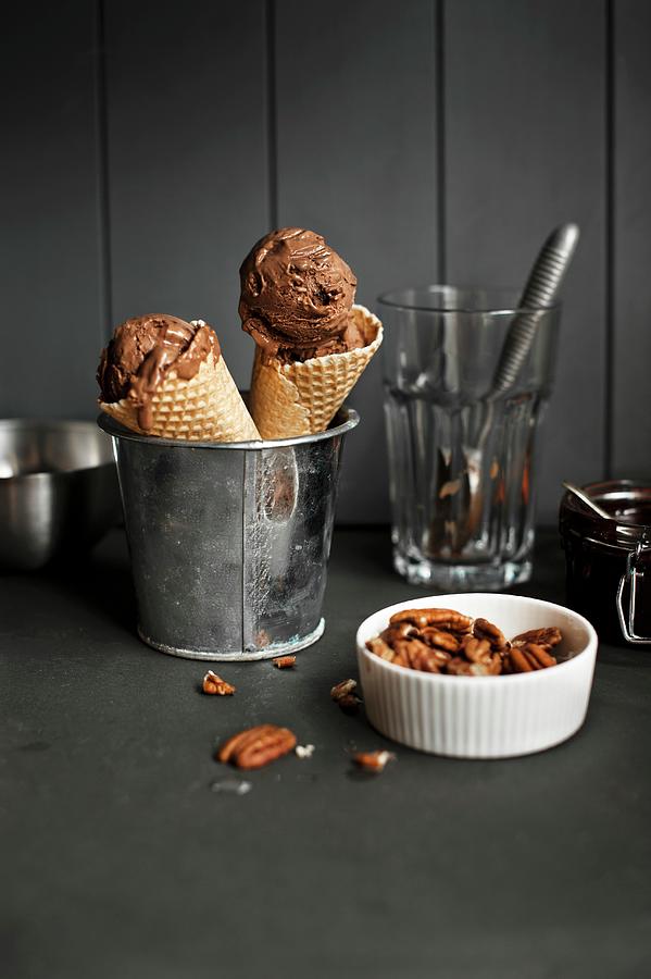 Two Cones Of Chocolate Ice Cream In A Metal Bucket Next To A Bowl Of Pecan Nuts Photograph by Magdalena Hendey