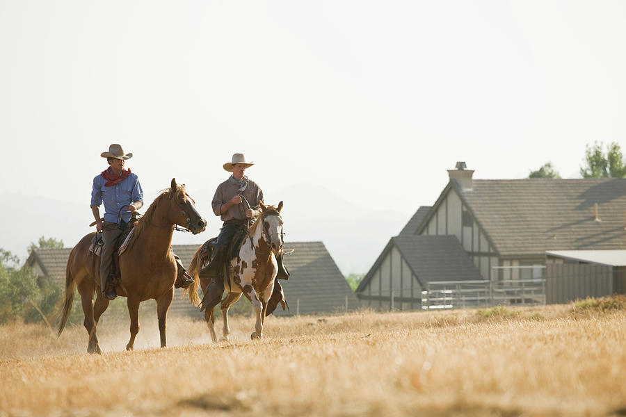 Two Cowboys Riding Horses Through A Photograph by Adam Burn