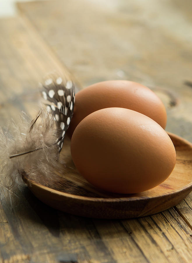 Two Fresh Eggs In A Wooden Dish And A Spotty Feather On A Rustic Wooden Table Photograph by Stacy Grant