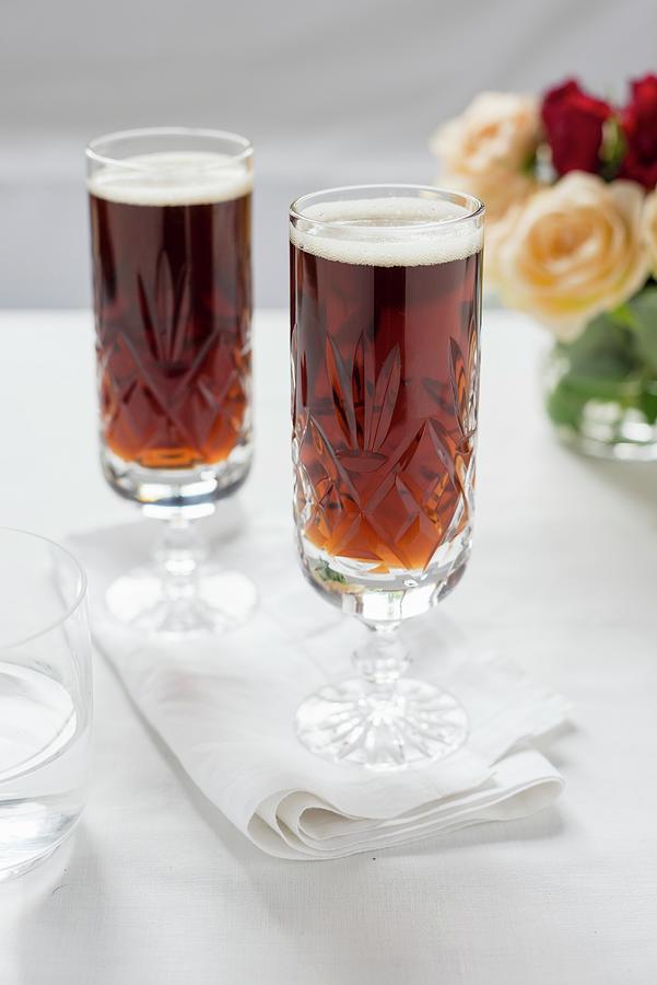 Two Glasses Of Dark Beer With A Bunch Of Roses In The Background Photograph by Sarka Babicka