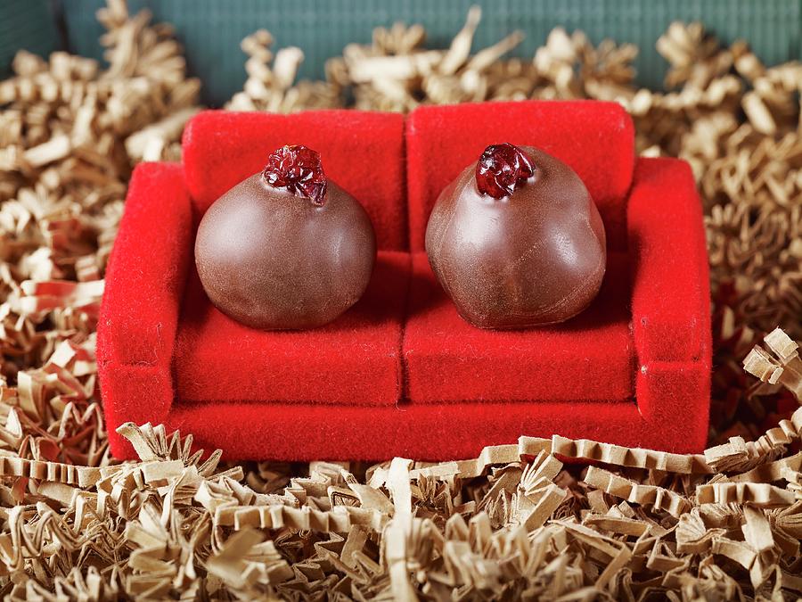 Fruit Photograph - Two Handrolled Marzipan Truffles In Dark Chocolate With Cranberries As Coach Potatoes On A Red Sofa by Foto4food