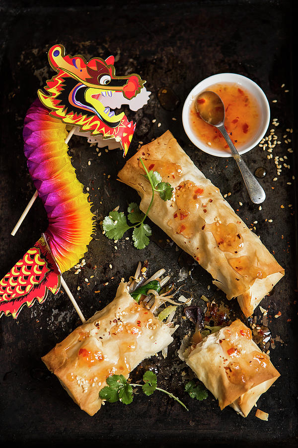 Two Homemade Vegetable Spring Rolls One Torn Open Sprinkled With Chilli Flakes And Sesame Seeds And Fresh Coriander With Sweet Chilli Sauce And A Celebration Paper Dragon Photograph by Stacy Grant