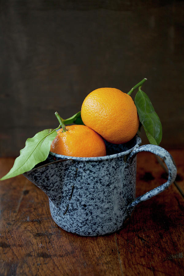 Two Oranges In An Antique Blue Enamel Jug, Sitting On A Wooden Tabletop Photograph by Ryla Campbell