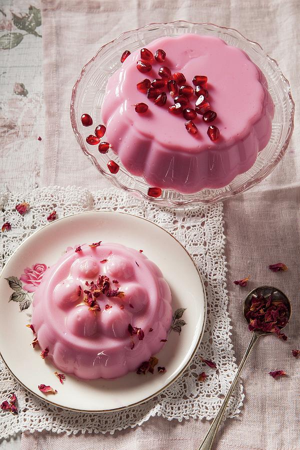 Two Pastel Pink Milk Jellies On Vintage Glass Cake Stand And Plate One Covered With Pomegrante Seeds The Other With Dried Rose Petals Shot Overhead On Vintage Lace Napkin Photograph by Stacy Grant