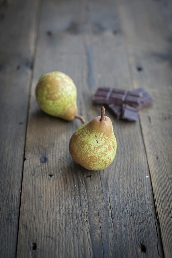 Two Pears And Pieces Of Chocolate On A Wooden Surface Photograph by Anne Faber