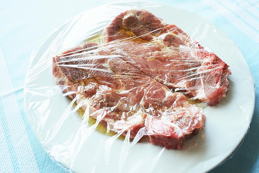 Two Pork Collar Steaks In Olive Oil Marinade On A White Plate Under Cling Film Photograph by Lippert, Oliver