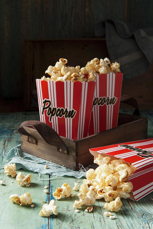 Two Red And White Striped Boxes Of Popcorn On A Wooden Tray One Box Tipped Over With Popcorn Spilling Out Onto An Aqua Green Blue Wooden Surface Photograph by Stacy Grant