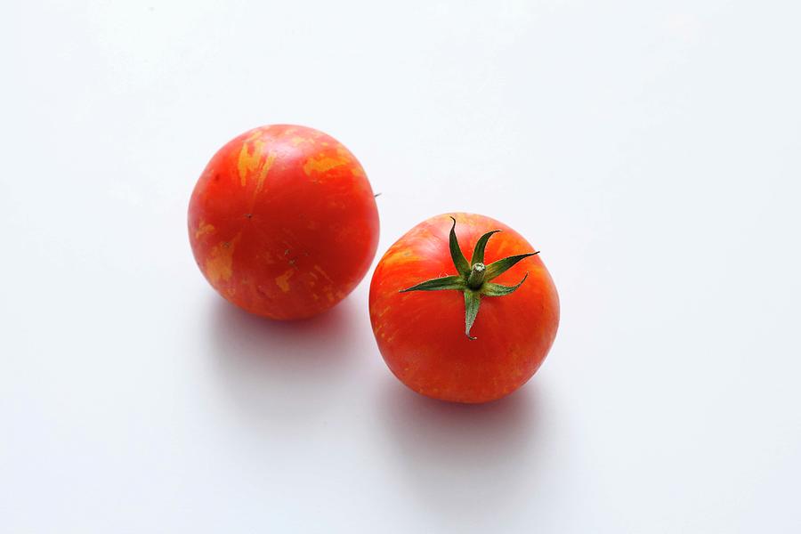Two Red Striped Tomatoes On A White Surface Photograph by Jalag / Mathias Neubauer
