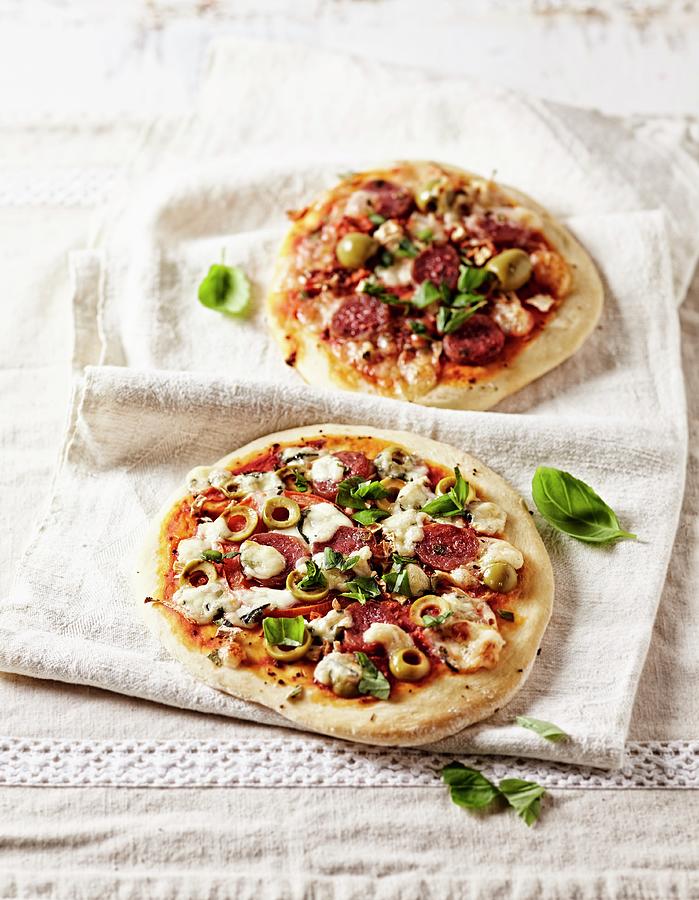 Two Rustic Pizzas With Chorizo, Green Olives And Basil Leaves Photograph by B.&.e.dudzinski