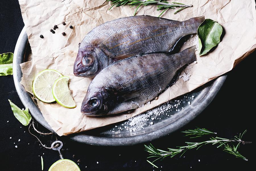 Two Seabream Fish With Rosemary, Lime And Sea Salt Server On Baking Paper Photograph by Natasha Breen