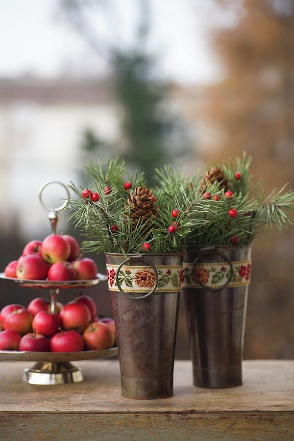 Two Small Metal Buckets Decorated With Vintage Ribbons, Spruce Twigs And Pine Cones In Front Of Red Apples On Cake Stand Photograph by Alicja Koll
