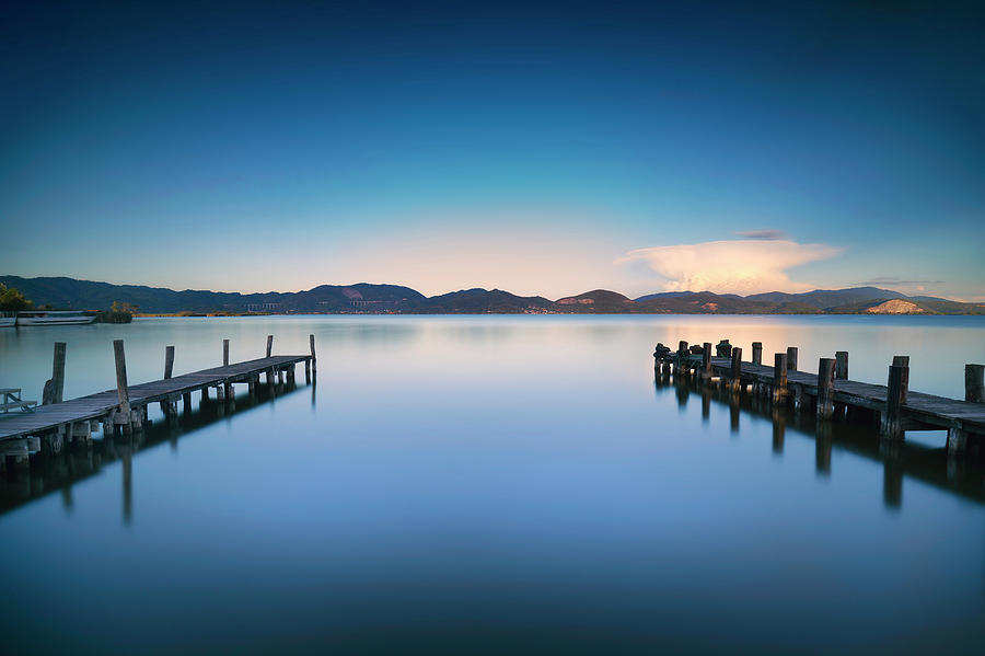 Two Wooden pier or jetty and on a blue lake sunset and sky refle Photograph by Stefano Orazzini