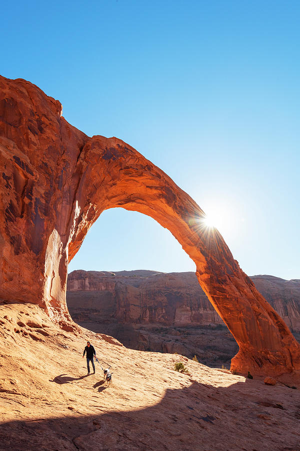 United States, Utah, Arches National Park, Corona Arch, Man Walking His Dog Under Corona Arch Digital Art by Jordan Banks