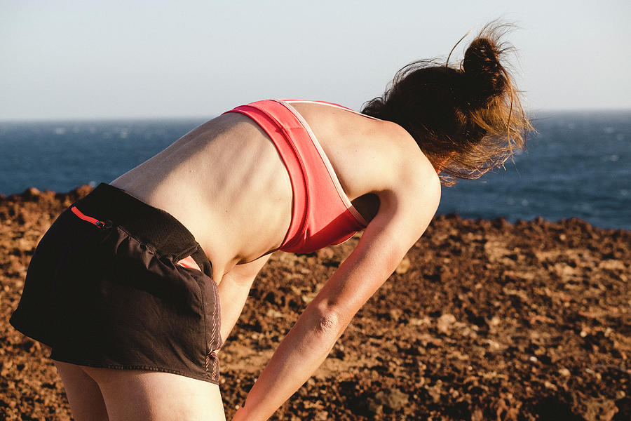 Sunset Photograph - Upper Body Back View Of Female Runner Having A Rest By The Sea by Cavan Images
