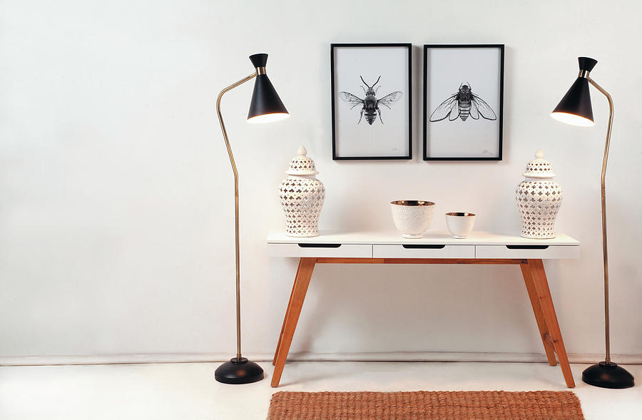 Urns On Console Table Flanked By Two Standard Lamps Below Drawing Of Insects On Wall Photograph by Great Stock!