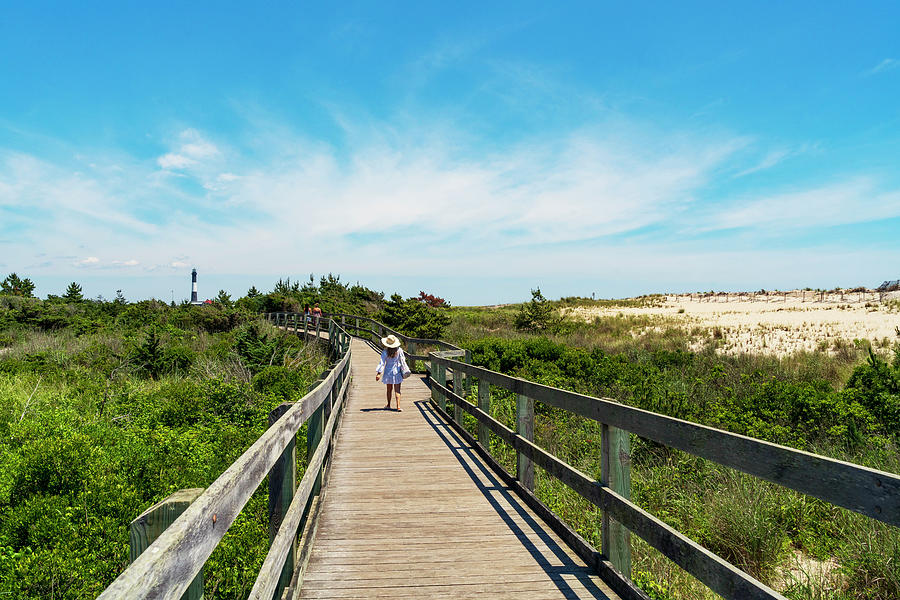 Usa, New York, Long Island, Woman Walking On A Wooden Path To Fire Island Lighthouse Surrounded By Tall Grass And Sand. Digital Art by Alejandra Uribe Posada
