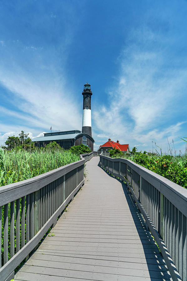Usa, New York, Long Island, Wooden Path Leading To Fire Island Lighthouse Surrounded By Tall Grass And Blue Sky. Digital Art by Alejandra Uribe Posada