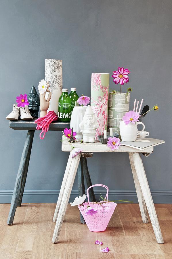 Utensils Such As Rolls Of Wallpaper, Bottles And Vases Decorated With Cosmos Flowers On Rustic Stools Against Grey Background Photograph by Cornelia Weber