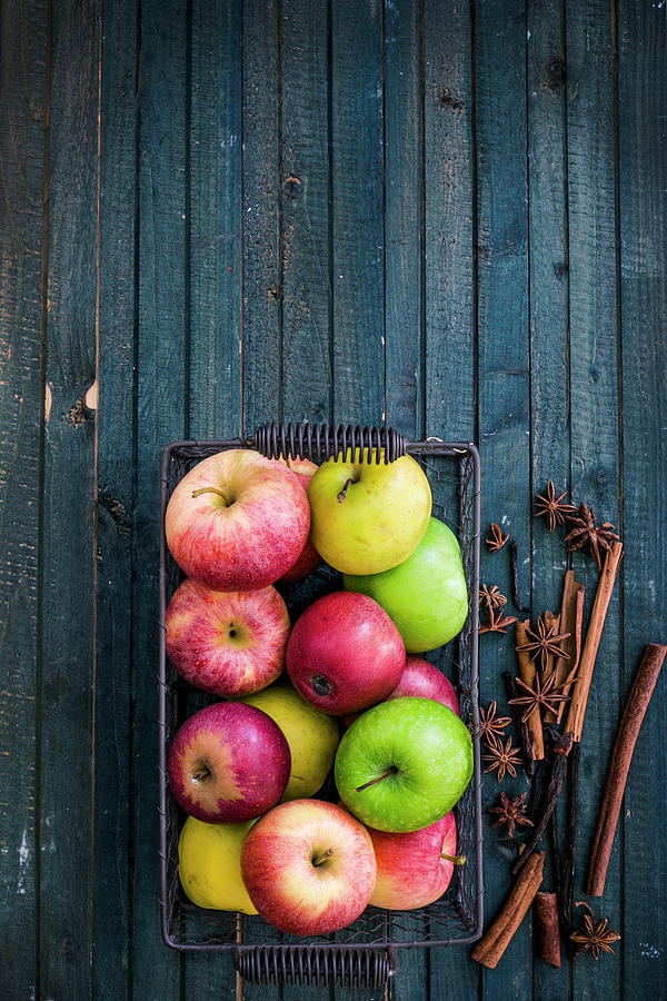 Various Apples In A Wire Basket And Spices On A Blue Wooden Background Photograph by Maricruz Avalos Flores