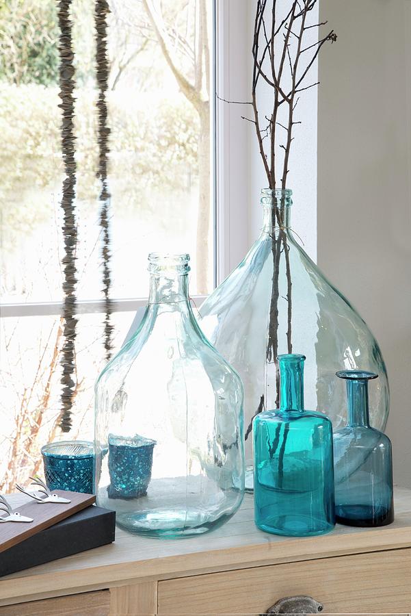 Various Clear And Blue Glass Bottles And Twigs In Front Of Window Photograph by Inge Ofenstein