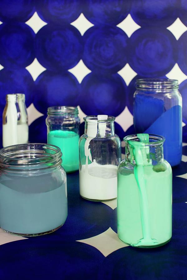Various Paints In Glass Jars On Length Of Blue Patterned Wallpaper Photograph by Annette Nordstrom