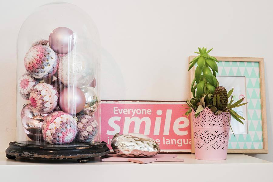Various Pastel Christmas Baubles With Crocheted Covers Under Vintage Glass Cover Next To Pink Enamel Sign And Plant On Surface Photograph by Bildhbsch
