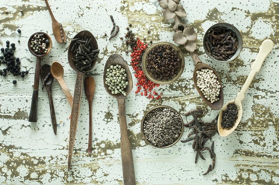 Various Types Of Pepper On Spoons And In Small Bowls On A Wooden Background Photograph by Achim Sass