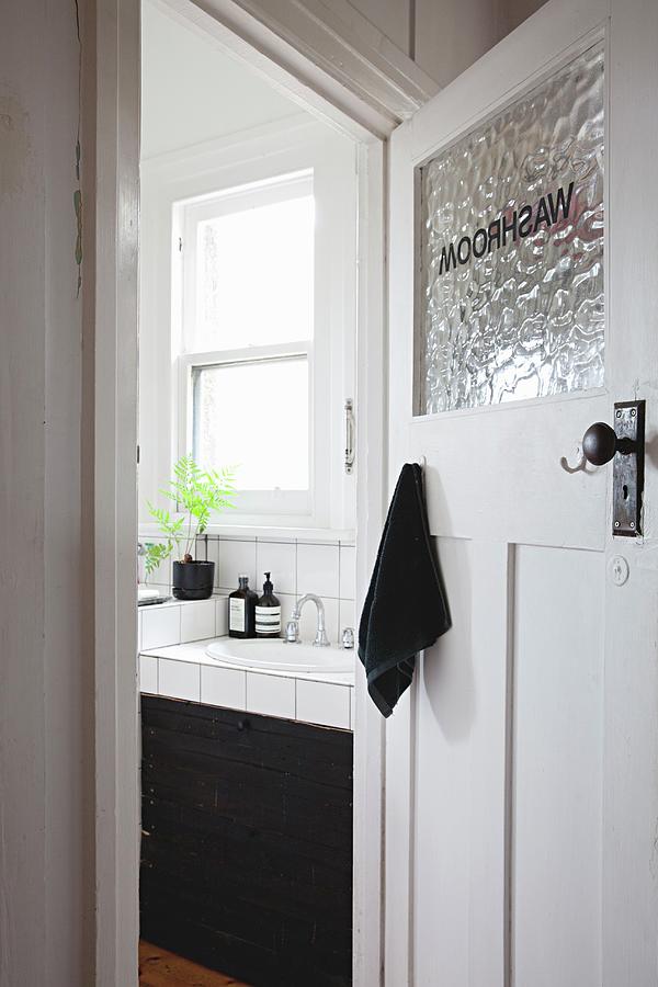 View Of Tiled Washstand With Black Base Unit Seen Through Open Bathroom Door In Period Apartment Photograph by Natalie Jeffcott