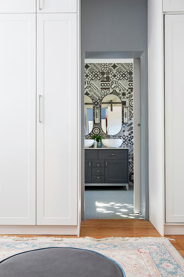 View Through Doorway Flanked By Wardrobes Into Bathroom With Grey Washstand Against Ornate Wall Tiles Photograph by Great Stock!