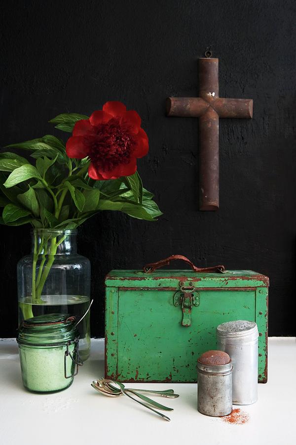 Vintage Kitchen Utensils In Front Of Green Metal Case And Red Flower In Vase And Cross Hanging On Black Wall Photograph by Sandra Eckhardt