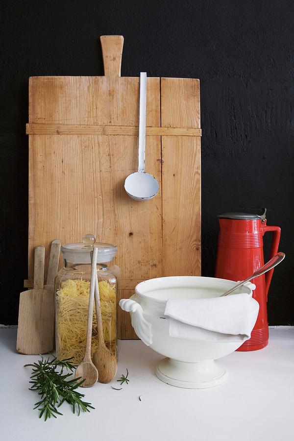 Vintage Soup Tureen And Pasta In Storage Jar In Front Of Chopping Board Leaning On Black Wall Photograph by Sandra Eckhardt