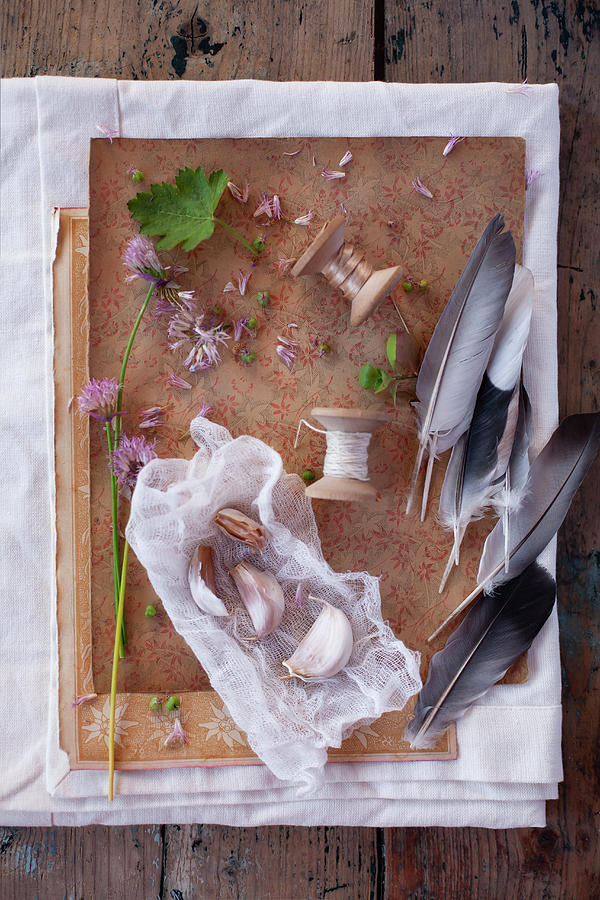 Vintage-style Arrangement Of Garlic Cloves, Flowers, Wooden Reels And Feathers Photograph by Alicja Koll