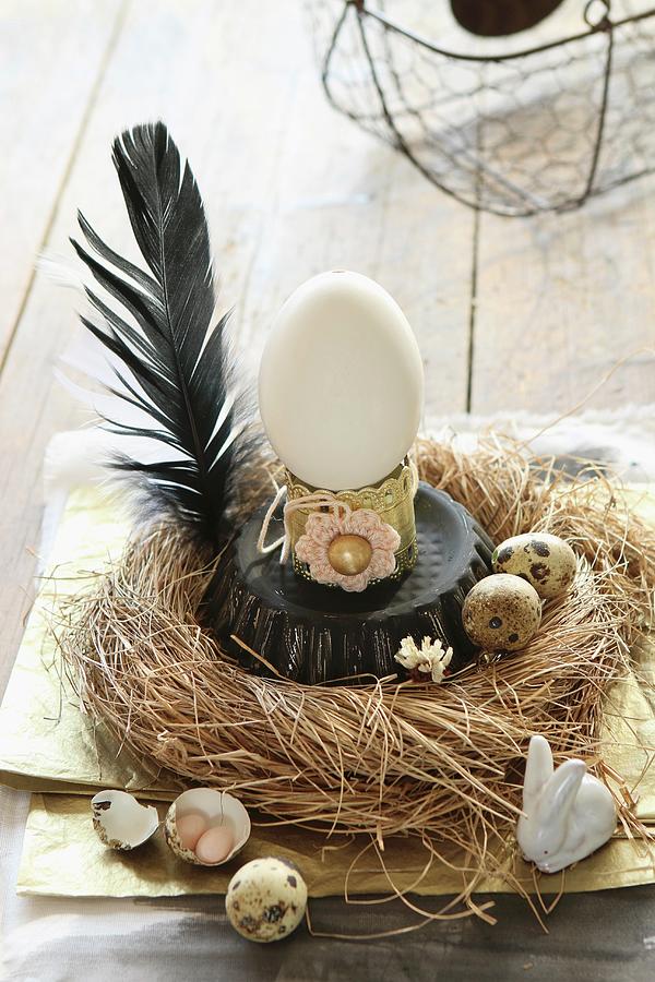 Vintage-style Easter Arrangement Of Ducks Egg On Upturned Cake Tin In Straw Nest With Quails Eggs And Black Feather Photograph by Regina Hippel