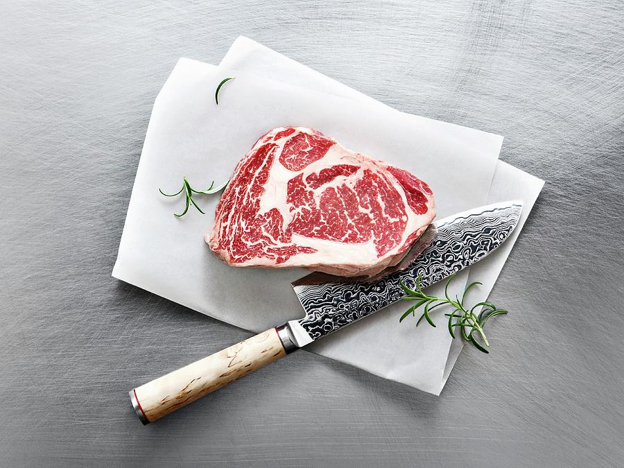 Wagyu Ribeye Steak With Rosemary And A Knife On A Piece Of Parchment Paper Photograph by Thorsten Kleine Holthaus