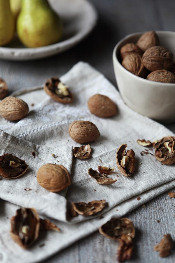 Walnuts And Walnut Shells On A Cloth With A Plate Of Pears In The Background Photograph by Sabrina Sue Daniels