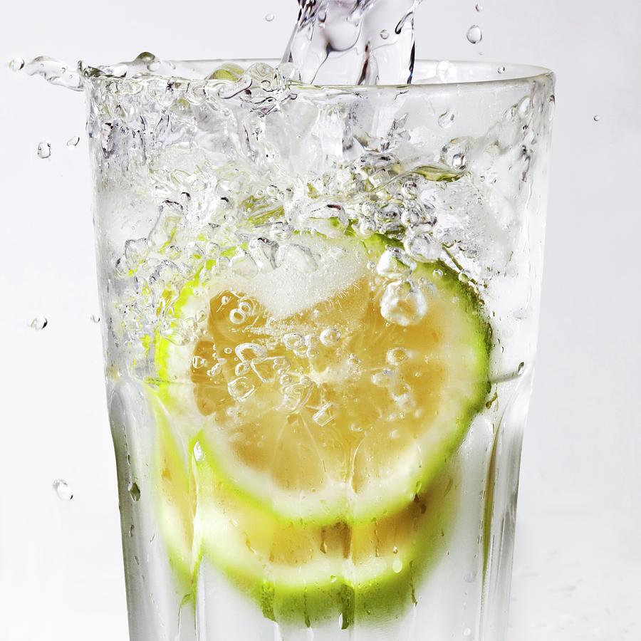Water Being Poured Into A Glass Of Lime Slices Photograph by Uwe Merkel