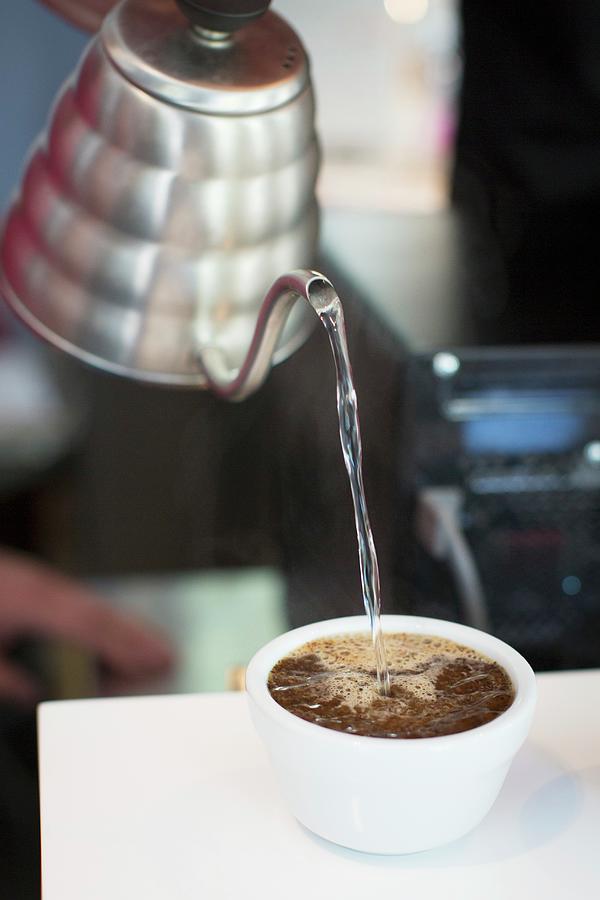 Water Being Poured Into Cup Of Coffee Beans Photograph by Anne Faber