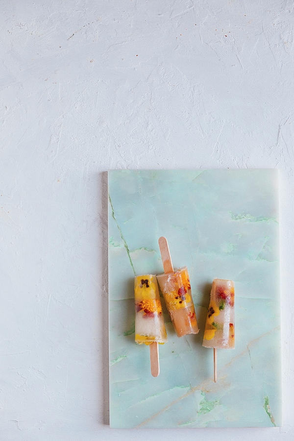 Water Icecreams With Elderflower Syrup And Eatable Flowers On A Marble Plank And A White Backdrop Photograph by Lucie Beck