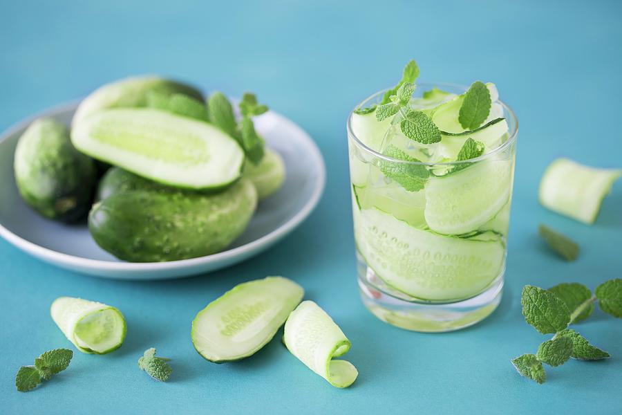 Water With Cucumber Strips, Mint And Ice On A Blue Surface Photograph by Malgorzata Laniak
