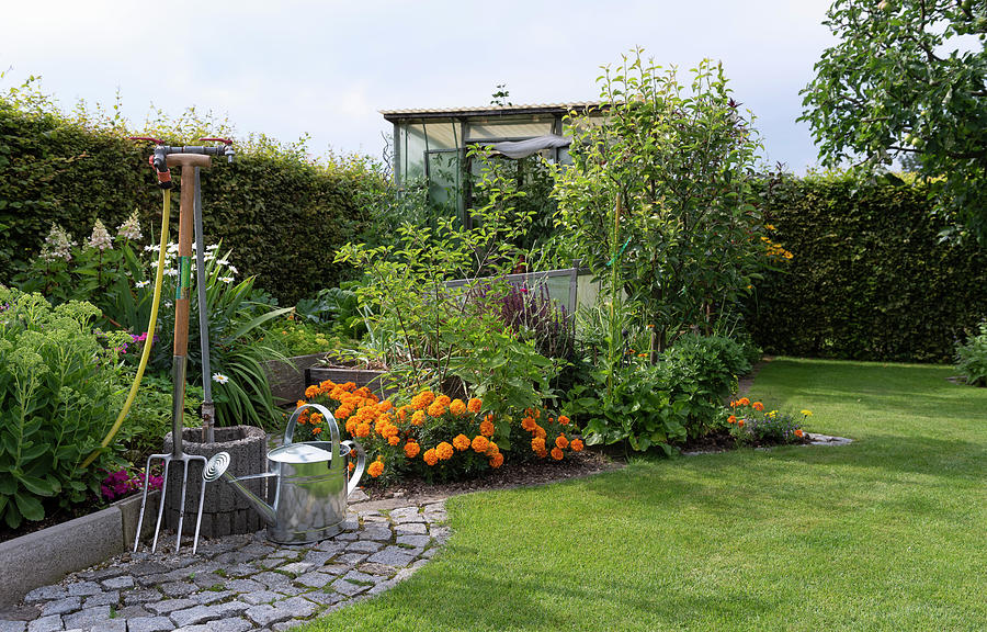 Watering Hole In The British Garden, Watering Can And Pitchfork, View Of The Flower Bed And Greenhouse. Photograph by Ira Hilger