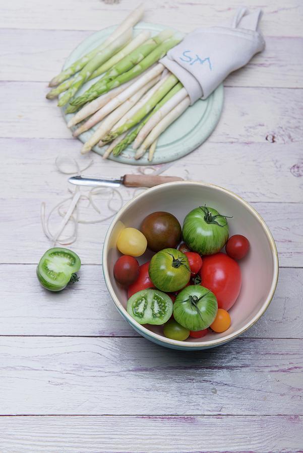 White And Green Asparagus On A Wooden Board, Asparagus Peelings, A Peeler And A Bowl Of Various Tomatoes Photograph by Angelika Grossmann