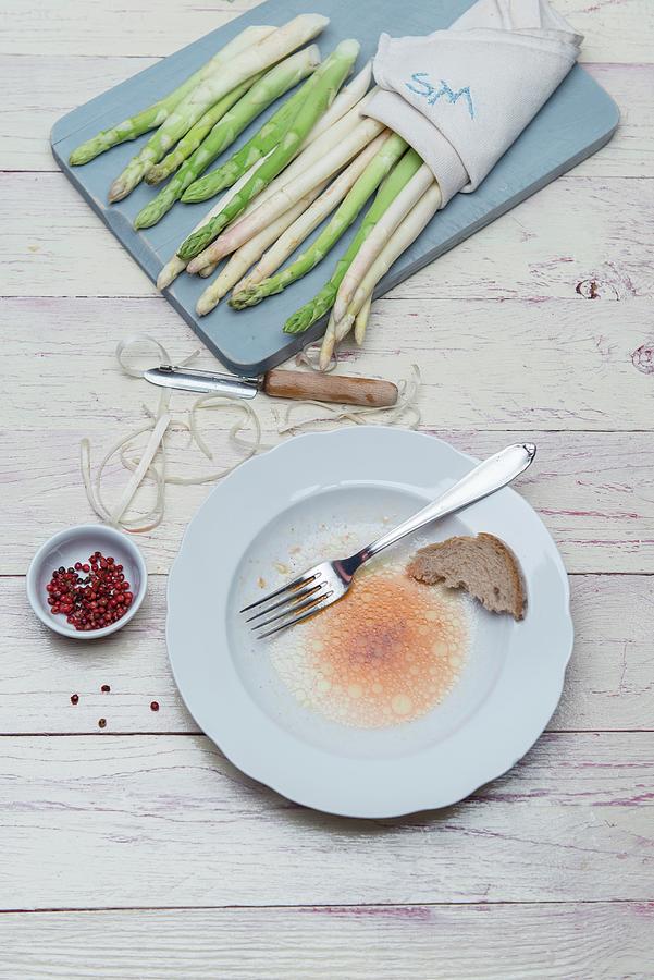 White And Green Asparagus On A Wooden Board With Peelings And A Peeler, The Remains Of Vinaigrette On A Plate With A Piece Of Bread And A Fork Photograph by Angelika Grossmann