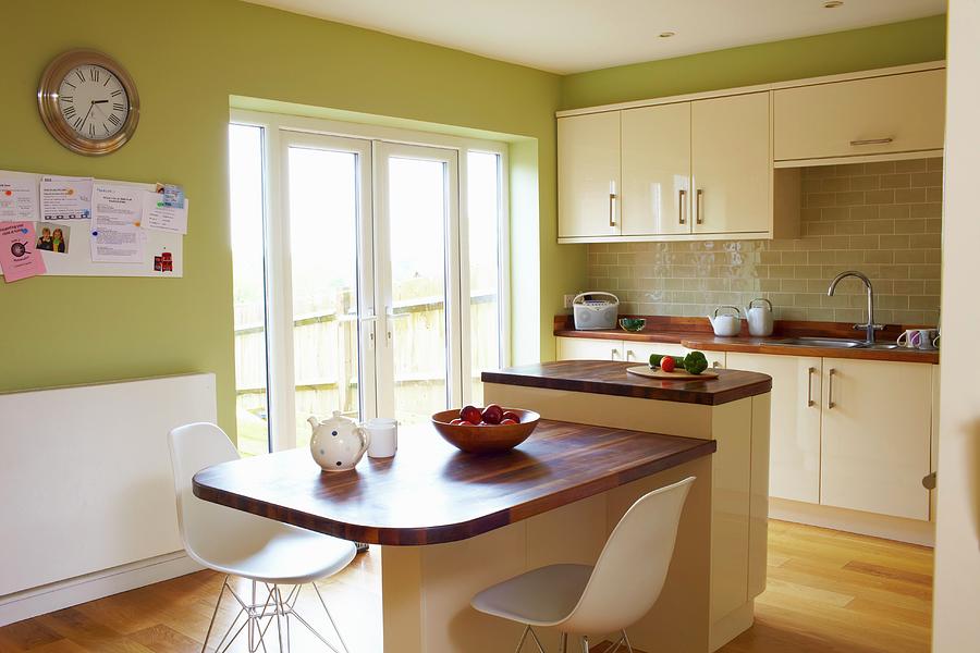 White Classic Shell Chairs At Table With Wooden Top Abutting Island Counter In Kitchen With Green-painted Walls Photograph by Tim Imri