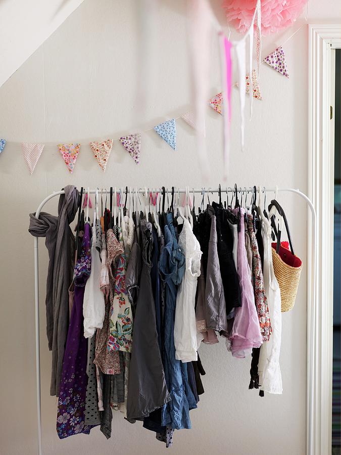 White Clothes Rail Holding Girls Clothing And Pastel Bunting Hung On Wall Photograph by Peter Carlsson