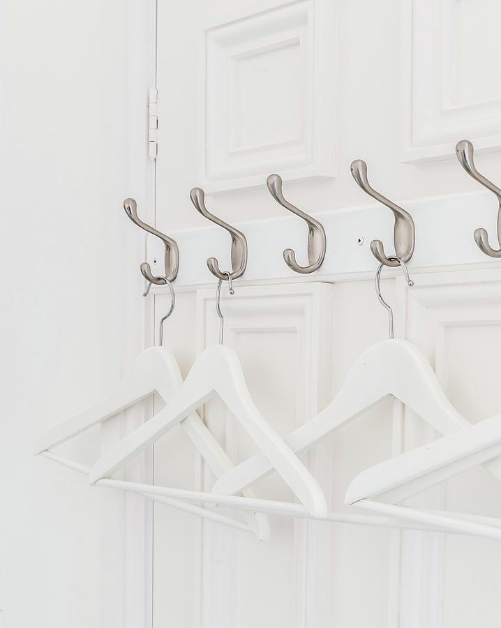 White Coathangers Hung From Row Of Hooks On Panelled Door Photograph by Stuart Cox