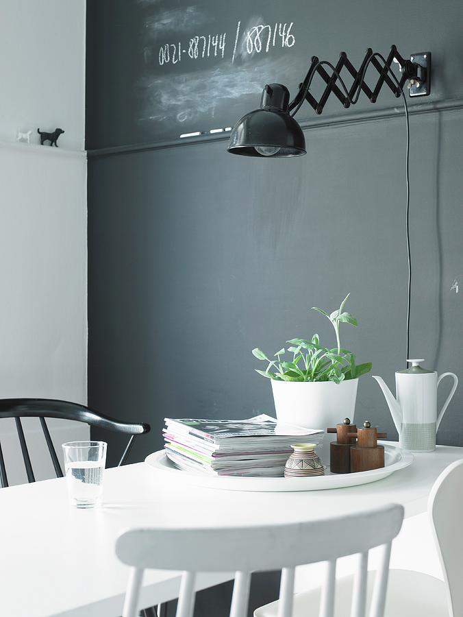 White Dining Table In Front Of Grey Wall With Retro-style, Black Wall Lamp Photograph by Stefan Thurmann
