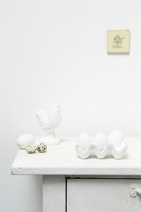 White Eggs In Egg Box, Quail Eggs And Cockerel Ornament On Top Of Cabinet Photograph by Thordis Rggeberg